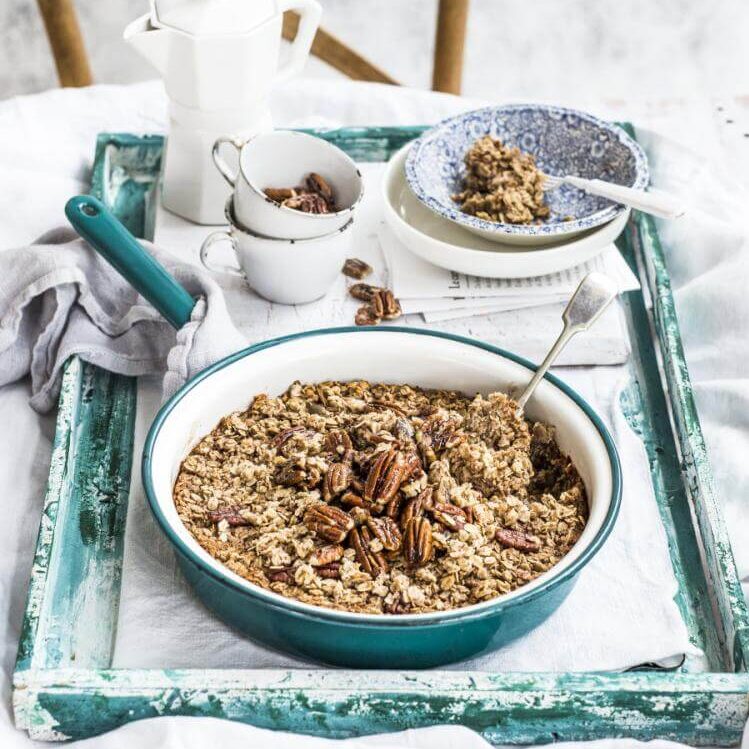 Baked gingerbread porridge with caramelised pecans in bowl on wooden teal painted tray