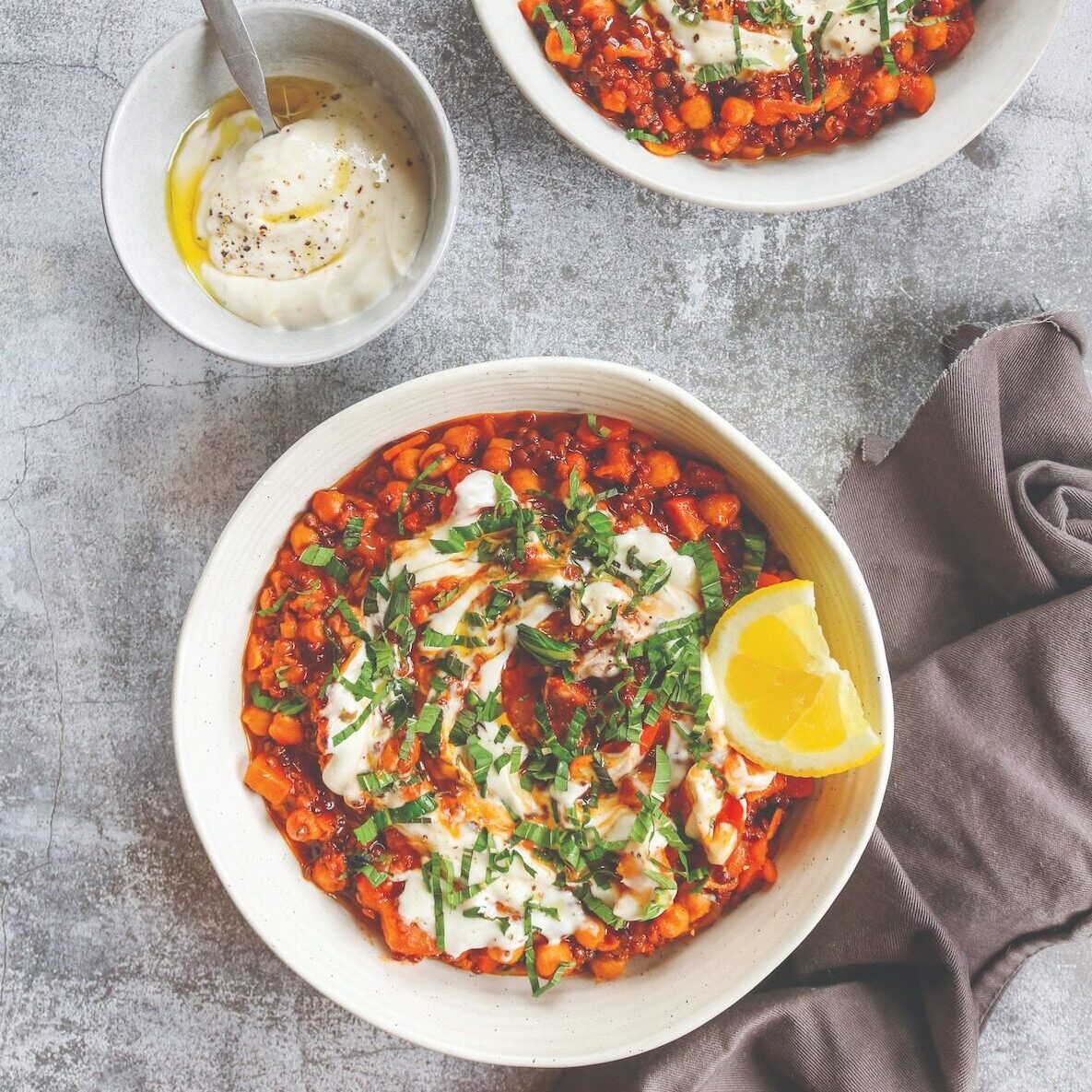 Tagine in two bowls on stone surface with vegan yoghurt sauce