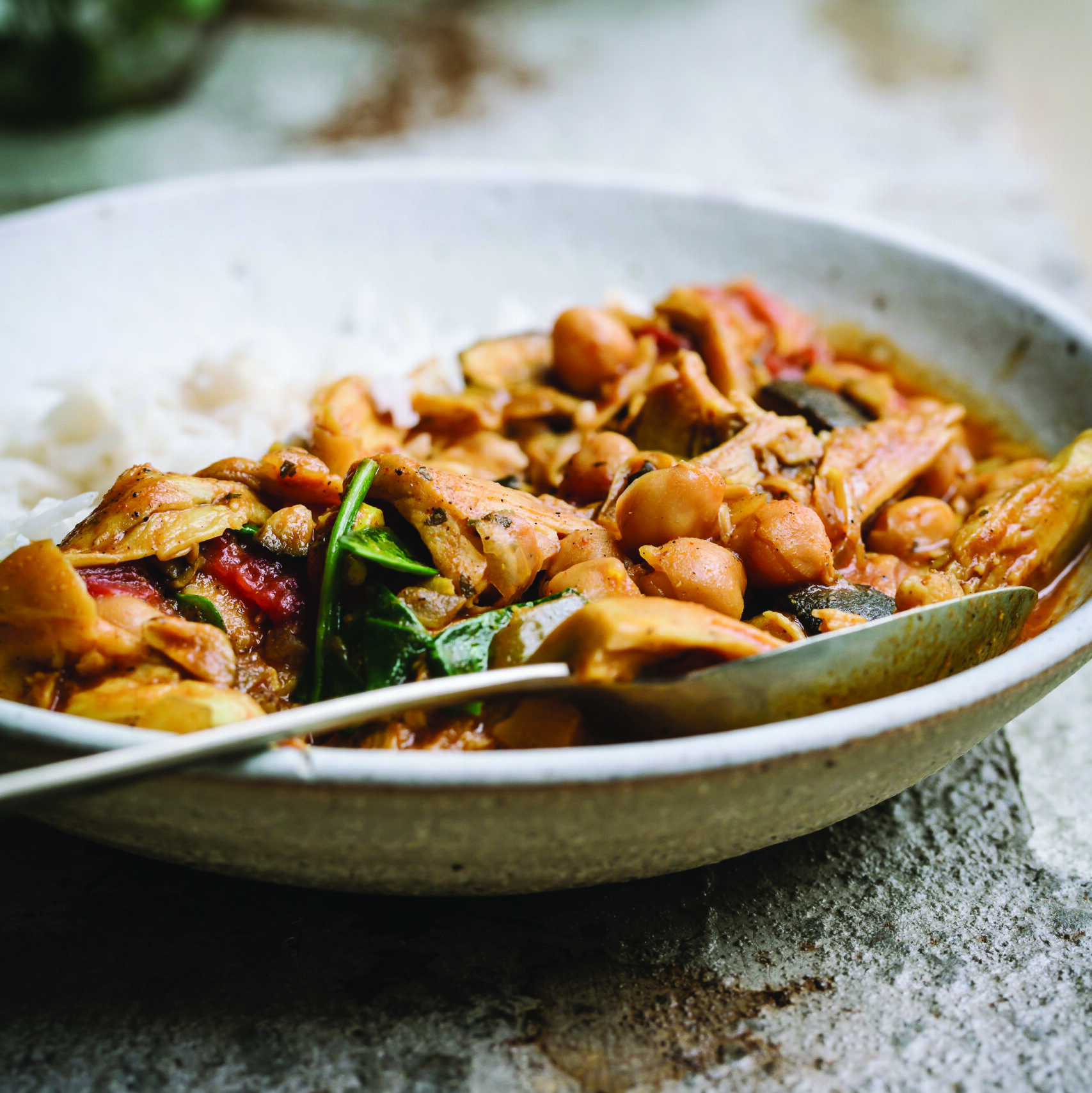 Tikka masala with rice in bowl, set on stone surface, with spoon in bowl