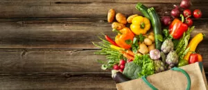 Hessian bag with healthy groceries (whole plant foods) spreading out onto wooden table