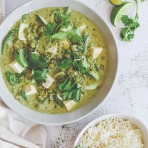 Bowl of green curry pictured from above on marble tabletop, with bowl of rice