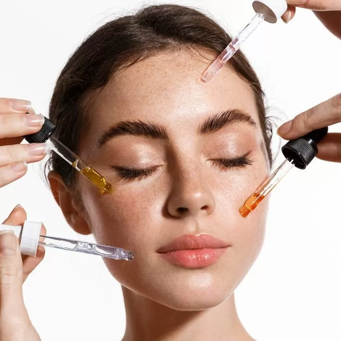 Skin care and rejuvenation. Beautiful Model With Radiant And Glowing Facial Skin Looking At Camera. Moisturizing With Serum Collagen And Hyaluronic Acid. Hands with serum dropper near girl face.