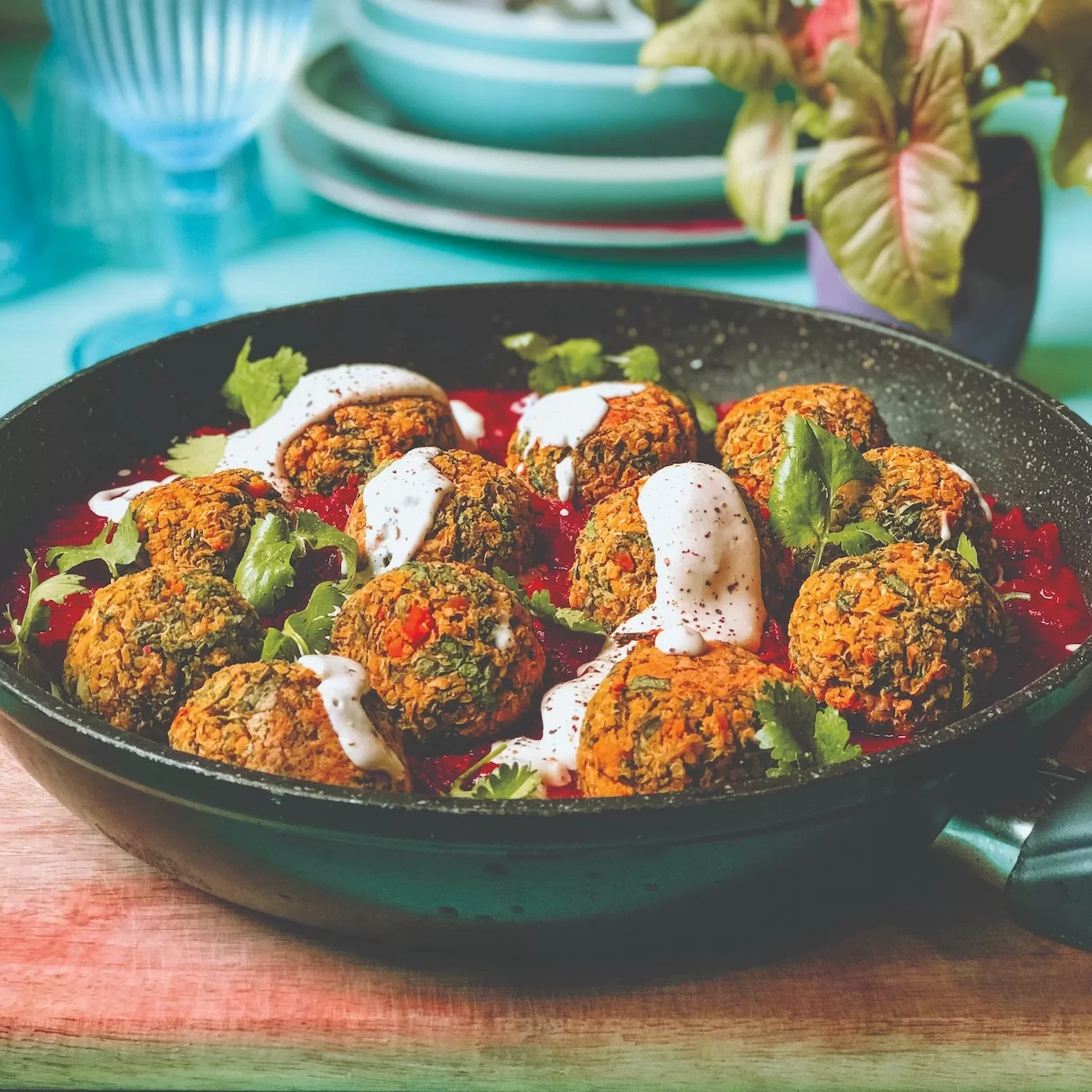 Chickpea balls in black shallow-sided bowl on table with pot plant and blue crockery in background