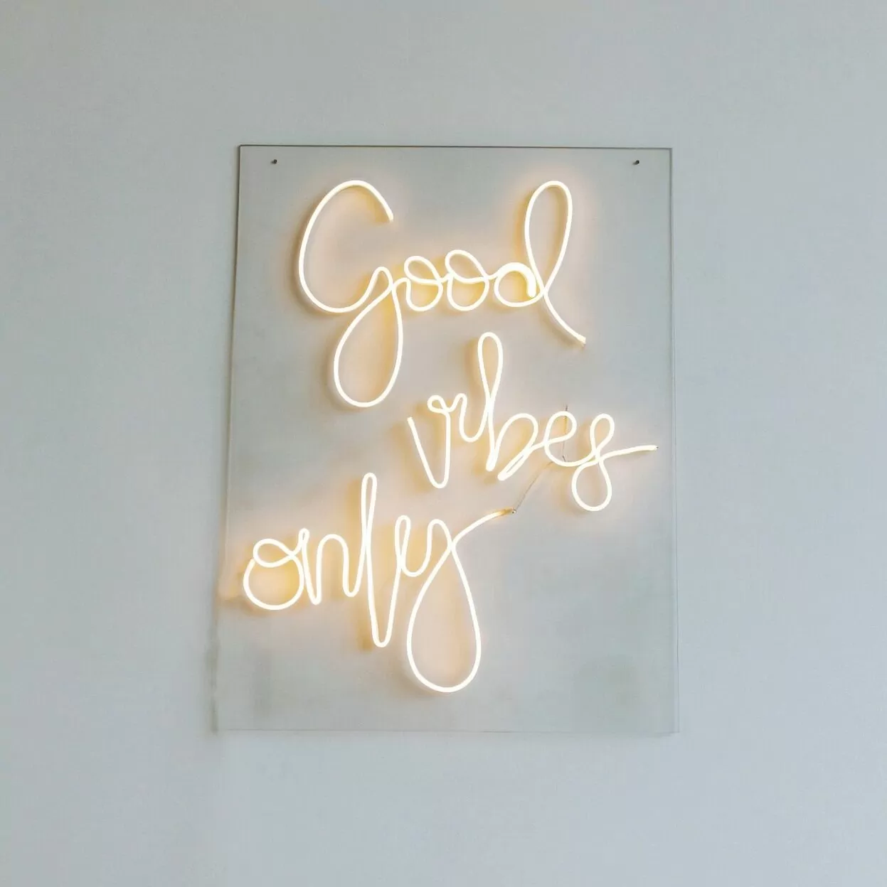 Neon 'good vibes only' sign in warm yellow on white wall
