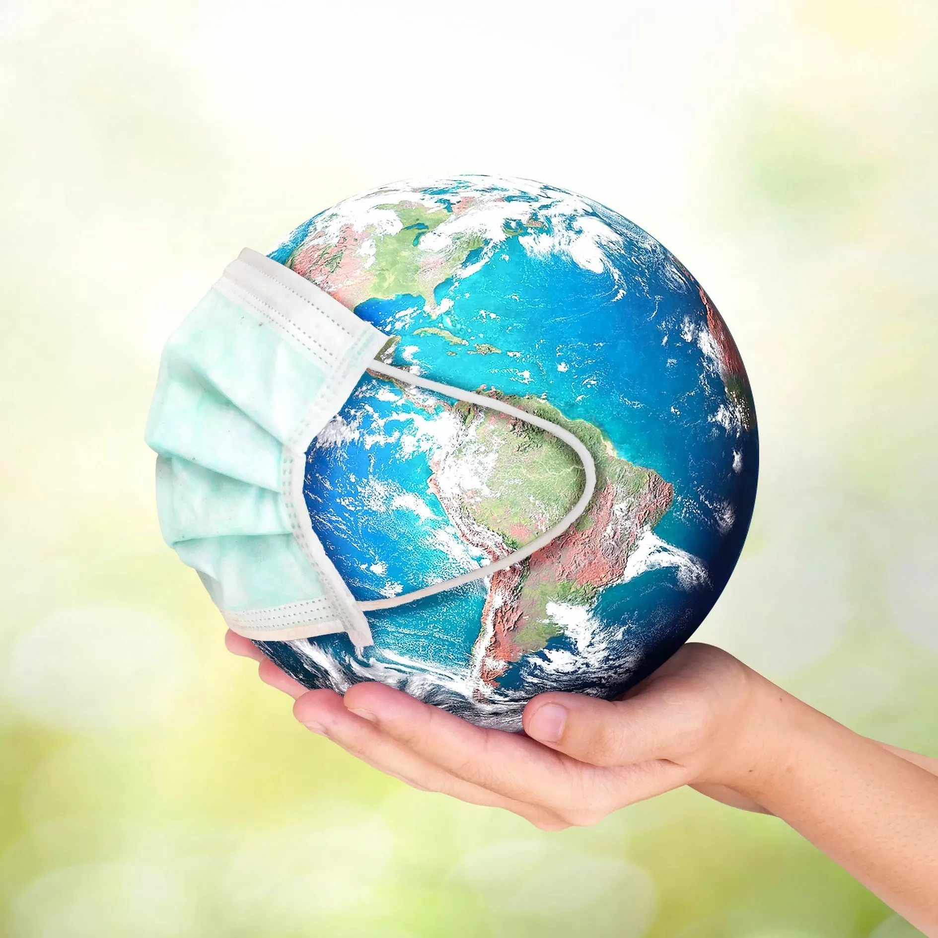 Hand holding up planet Earth, pictured wearing a pandemic mask