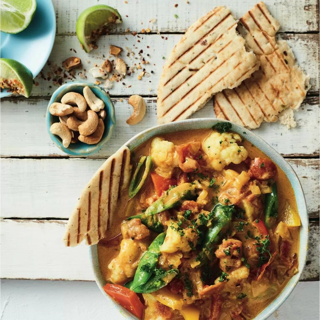 Creamy vegetable korma - in bowl on wooden table with lime wedges, breads, cashews